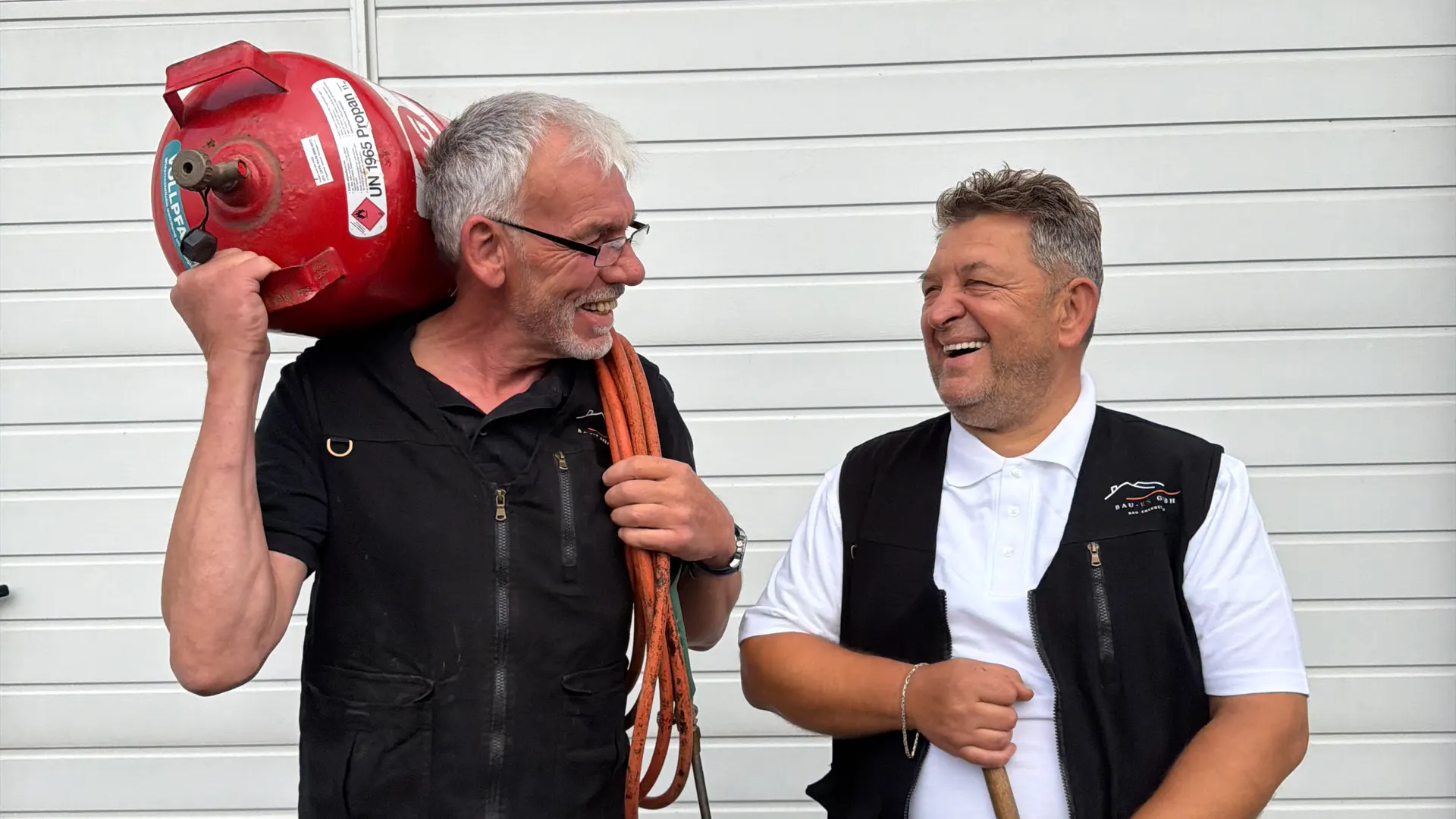 Zwei Kollegen der BAU-EN GmbH lachen bei der Vorbereitung ihrer Arbeitsgeräte